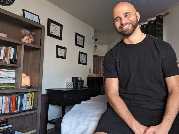 Male massage therapist seated in a professional treatment room.