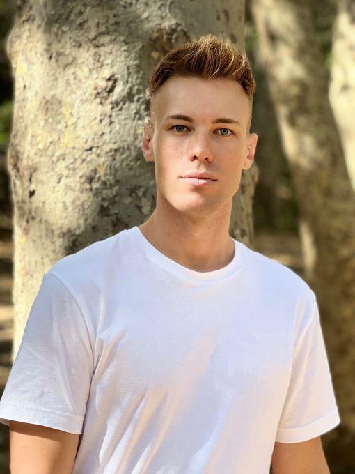 Fit young man standing outdoors in a white t-shirt near trees