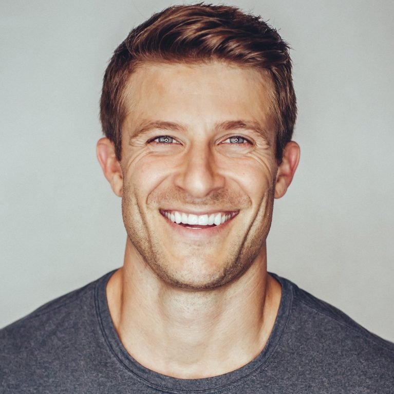 Smiling fit man with clear skin and relaxed expression against a neutral background