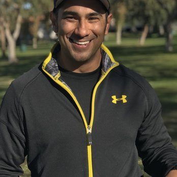 Athletic man in a black zip-up jacket standing outdoors in a park setting