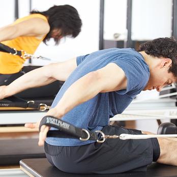 Male client performing controlled resistance training with straps under the supervision of a personal trainer in a studio setting